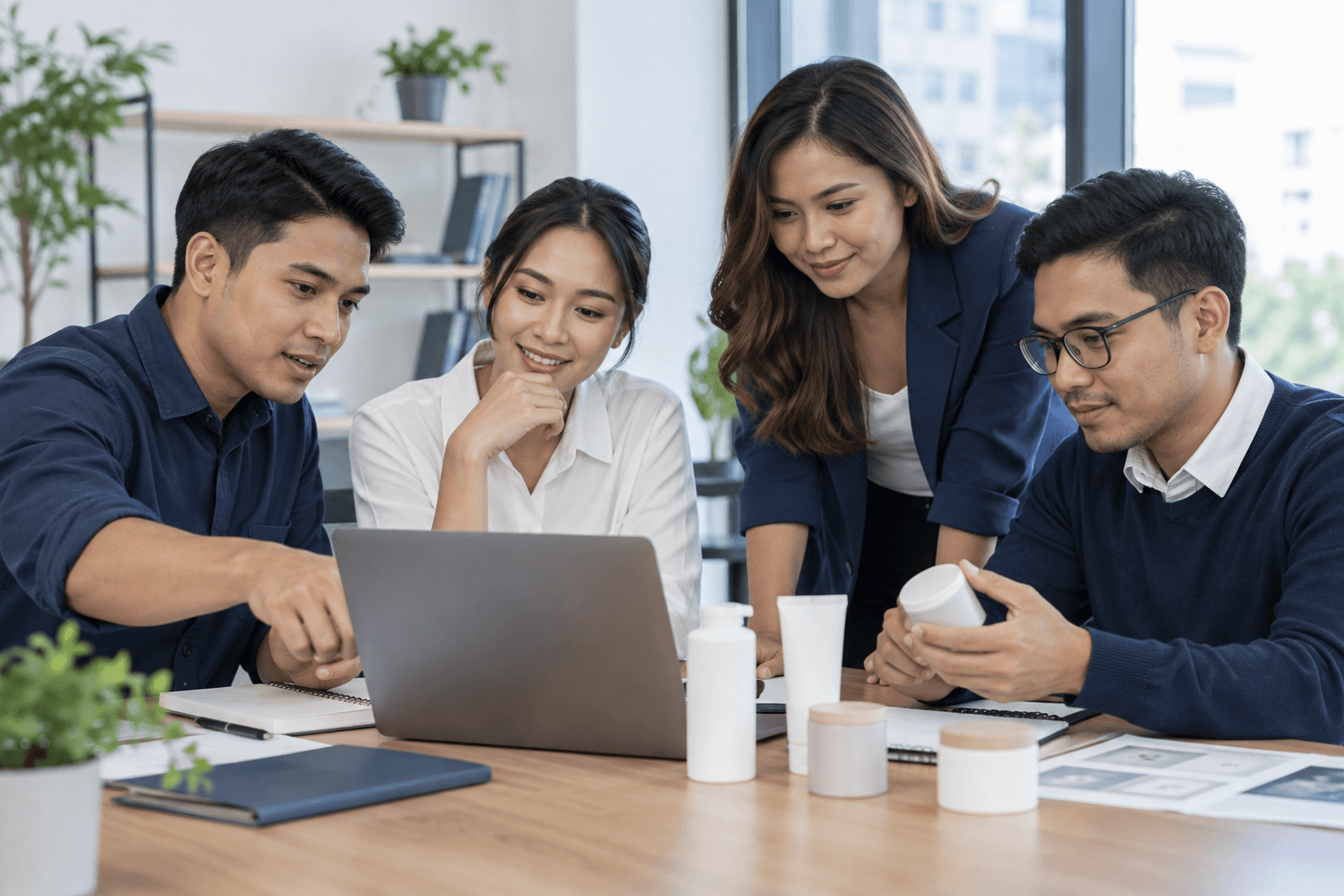 Four adult professionals discussing a laptop and unbranded product samples in a bright office